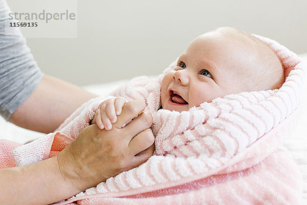 Kleiner Junge (12-17 Monate) in rosa Decke  der die Hand seiner Mutter hält und lächelt