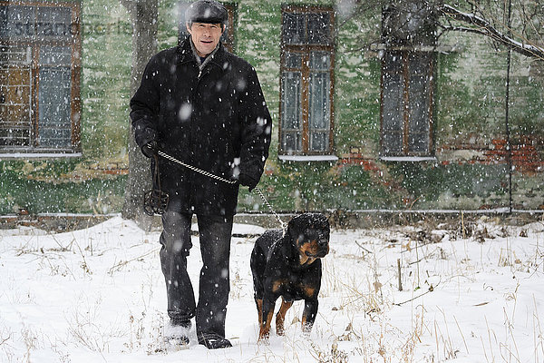 Ukraine  Dnepropetrovsk  Mann geht im Schnee mit Rottweiler