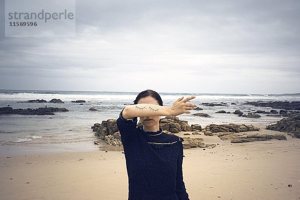Frau mit geschlossenen aufgemalten Augen auf ihrem Arm stehend am Strand  hinter dem Meer  Südafrika  Afrika