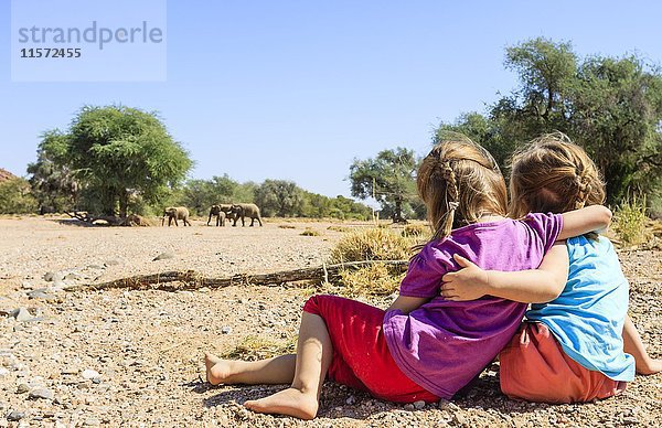 Zwei Mädchen beobachten Elefanten (Loxodonta africana) im Flussbett des Aba Huab  Damaraland  Kunene Region  Namibia  Afrika