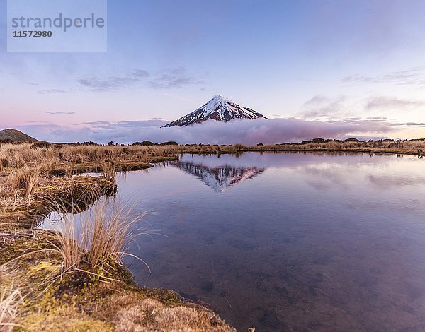 Spiegelung im Pouakai Tarn See  Wolken um den Stratovulkan Mount Taranaki oder Mount Egmont bei Sonnenuntergang  Egmont National Park  Taranaki  Neuseeland  Ozeanien