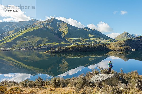 Wanderer auf Felsen stehend  Berge spiegeln sich im See  Moke Lake bei Queenstown  Region Otago  Southland  Neuseeland  Ozeanien