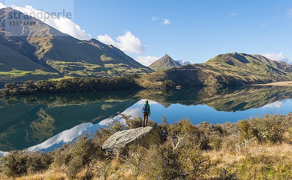 Wanderer auf Felsen stehend  Berge spiegeln sich im See  Moke Lake bei Queenstown  Region Otago  Southland  Neuseeland  Ozeanien
