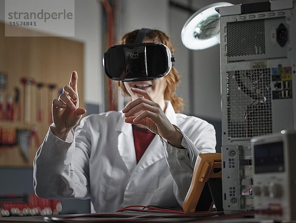 Frau mit VR-Brille und Laborkittel sitzt in einem Elektroniklabor  Österreich  Europa