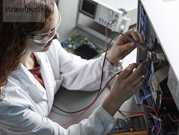 Ingenieur mit weißem Laborkittel und Schutzbrille misst Strom mit einem Messgerät  Österreich  Europa