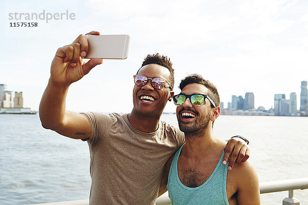 Zwei junge Männer beim Smartphone-Selfie am Wasser  New York  USA