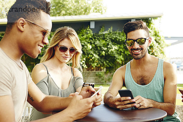 Männliche und weibliche Freunde lesen Smartphones am Parktisch