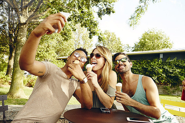 Männliche und weibliche Freunde nehmen Smartphone-Selfie beim Essen von Eistüten im Park