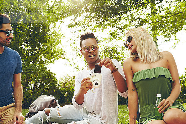 Junger Mann entfernt Film von Sofortbildkamera beim Picknick im Park