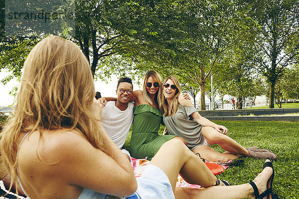 Über-Schulter-Ansicht einer Frau  die Freunde beim Picknick im Park fotografiert