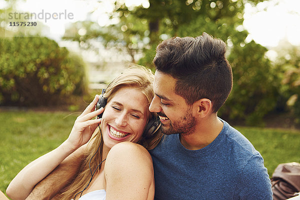 Junge Frau und Mann hören Kopfhörermusik im Park