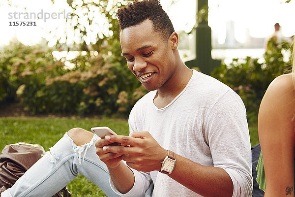 Junger Mann betrachtet Smartphone im Park sitzend