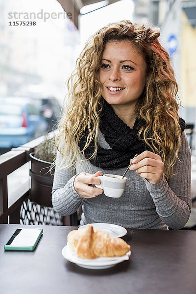 Frau im Café hält Espressotasse und schaut lächelnd weg.