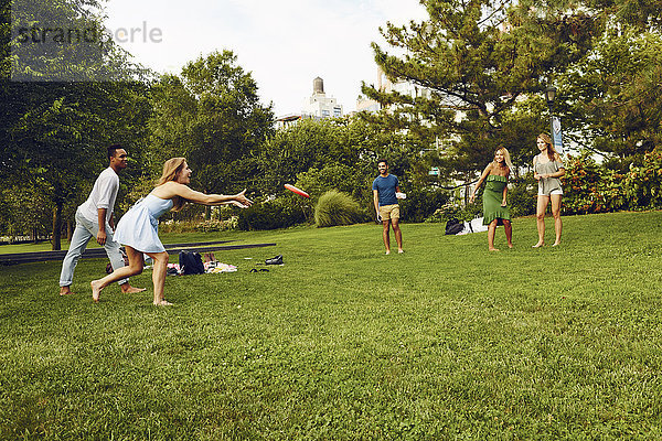 Fünf erwachsene Freunde spielen mit Flying Disc im Park