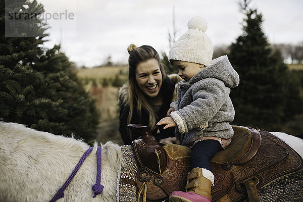 Mutter lächelt Baby Mädchen zu Pferd an