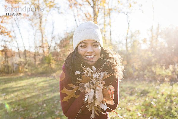 Porträt einer jungen Frau  die Herbstblätter hält