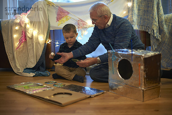 Junge und Großvater sitzen auf dem Boden und machen ein Roboterkostüm