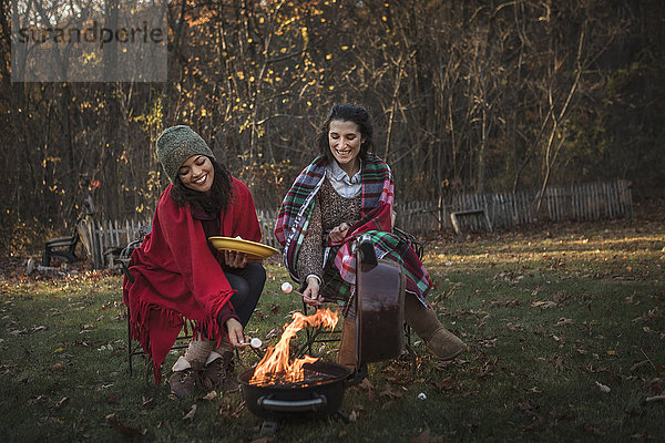 Zwei Freundinnen stoßen am Lagerfeuer auf Marshmallows an