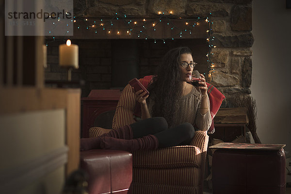 Junge Frau entspannt sich im Sessel und trinkt Rotwein