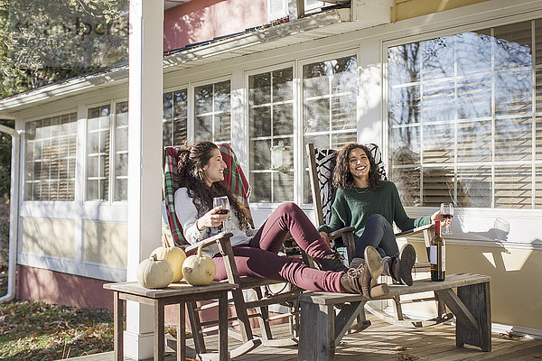 Zwei junge Freundinnen entspannen auf der sonnigen Terrasse bei Rotwein