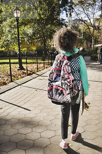 Rückansicht eines Mädchens mit Rucksack  das ein Skateboard trägt  New York  USA