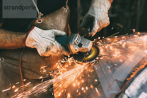 Hände eines Metallarbeiters beim Schleifen von Kupfer in einer Schmiedewerkstatt