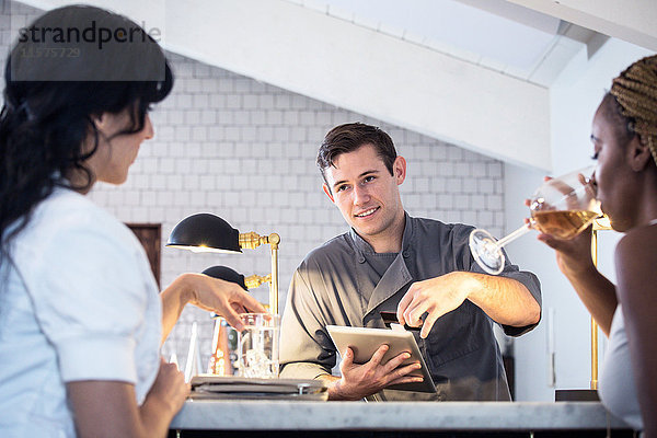 Barkeeper bedient Kunden an der Bar  Barkeeper nutzt digitales Tablett zur Zahlungsannahme