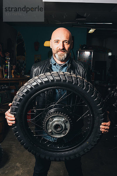 Porträt eines reifen Mannes in der Garage  der einen Motorradreifen hält