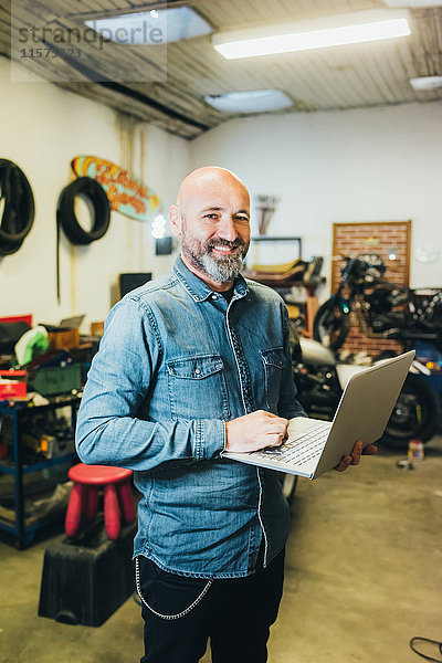 Porträt eines reifen Mannes  der in einer Garage arbeitet und einen Laptop benutzt