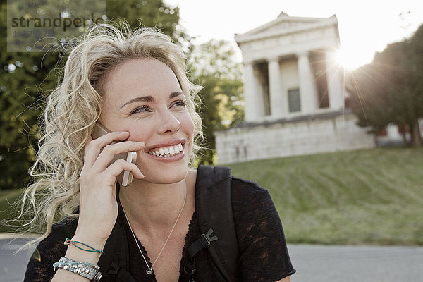 Mittelgroße erwachsene Frau im Park telefoniert mit einem Smartphone