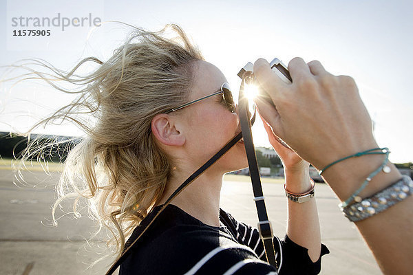 Mittelgroße erwachsene Frau mit fliegendem Haar  die mit einer Oldtimer-Kamera fotografiert
