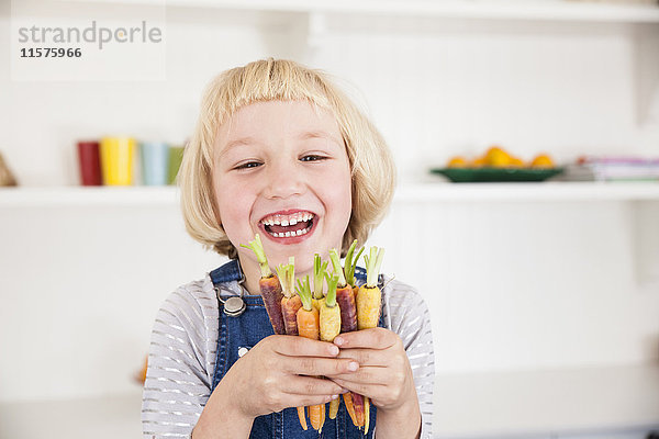 Porträt eines süßen Mädchens in der Küche  das einen Strauß bunter Karotten hält