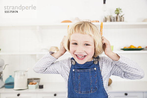 Porträt eines süßen Mädchens in der Küche  das Karotten an den Ohren hält