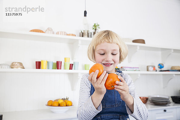 Geschnittenes Mädchen schaut sich in der Küche Orangen an