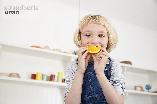 Porträt eines süßen Mädchens in der Küche  das eine Orangenscheibe an den Mund hält