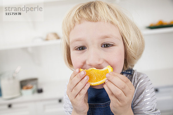 Porträt eines süßen Mädchens in der Küche  das eine Orangenscheibe an den Mund hält