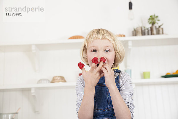 Porträt eines süßen Mädchens mit Himbeeren an den Fingern in der Küche