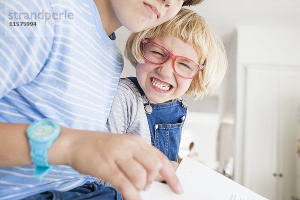 Mädchen zieht beim Lesen mit Bruder in der Küche das Gesicht