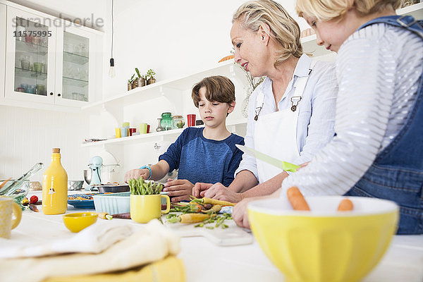 Reife Frau bereitet mit Sohn und Tochter Gemüse am Küchentisch zu