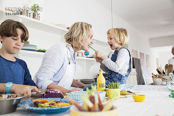 Mädchen füttert Mutter Spargel am Küchentisch