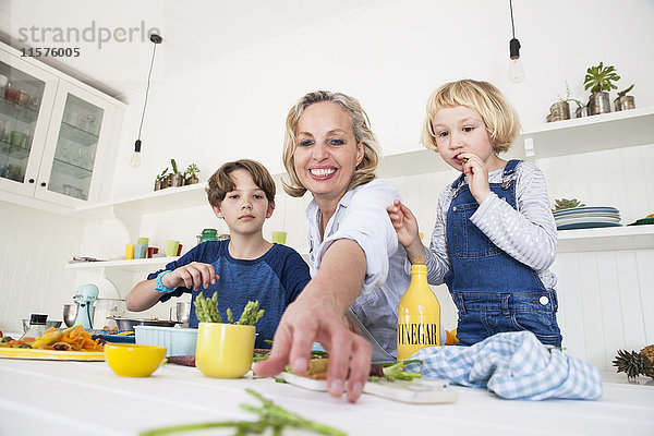 Reife Frau greift mit Sohn und Tochter am Küchentisch nach Spargel