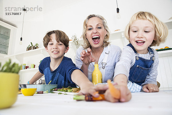 Mädchen und Bruder greifen nach Gemüse  während sie mit der Mutter am Küchentisch Essen zubereiten