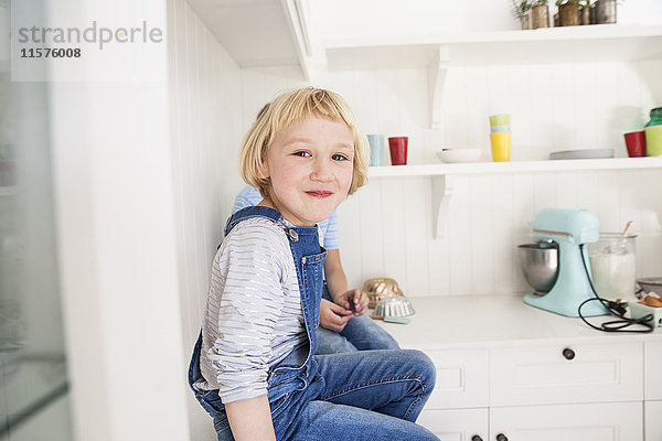 Porträt eines niedlichen Mädchens  das vor seinem Bruder auf dem Küchentisch sitzt