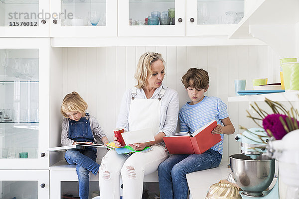 Reife Frau sitzt auf der Küchentheke und liest mit Sohn und Tochter Märchenbücher