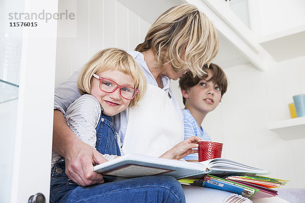 Reife Frau sitzt auf der Küchentheke und liest mit Sohn und Tochter Märchenbücher