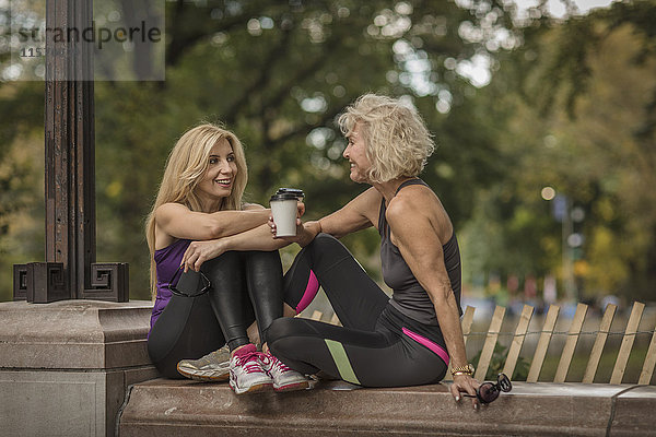 Zwei reife Freundinnen trainieren im Park  sitzen mit Kaffee zum Mitnehmen an der Wand