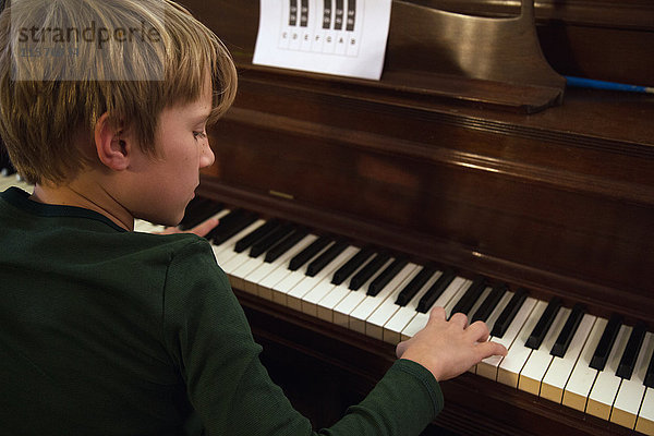 Über-Schulter-Ansicht eines Jungen  der im Wohnzimmer Klavier spielt