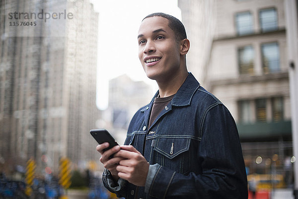 Junger Mann steht auf der Straße und benutzt ein Smartphone  Manhattan  New York  USA