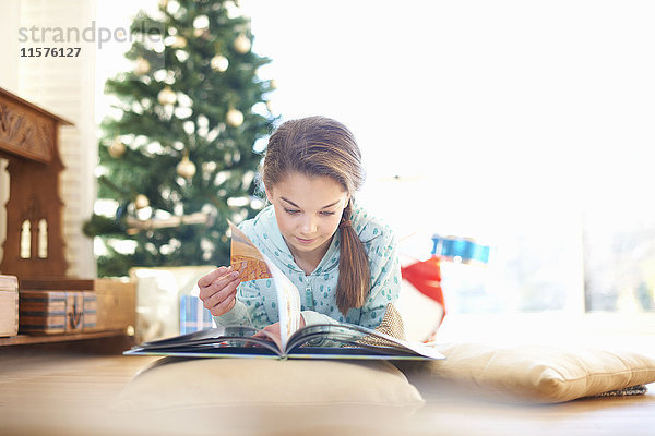 Mädchen liegt auf dem Wohnzimmerboden und liest zu Weihnachten ein Buch