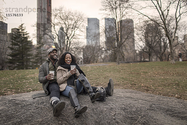 Ehepaar sitzt auf einem Felsen im Park mit Kaffee zum Mitnehmen